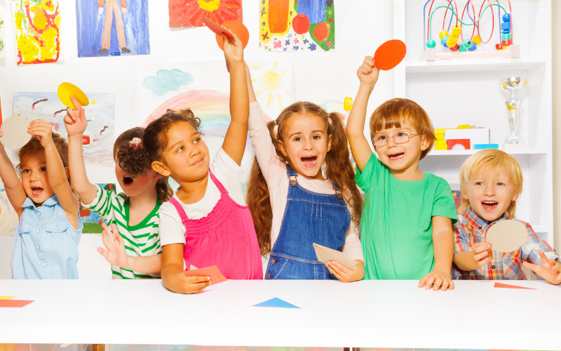 5 young students holding up shapes during a lesson.