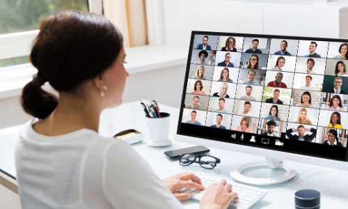 woman is facing desktop computer with gallery view of 36 other adults on a virtual meeting