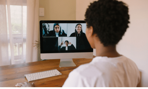 woman is looking at a computer monitor and talking to 3 other woman who are in gallery view on the screen