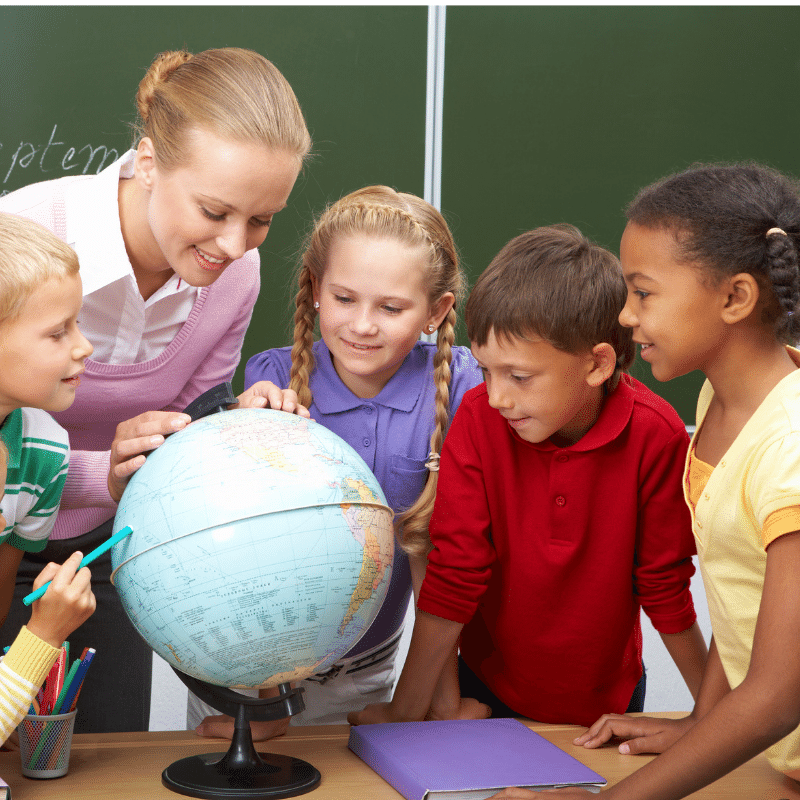 four young students and a female teacher are looking at a globe