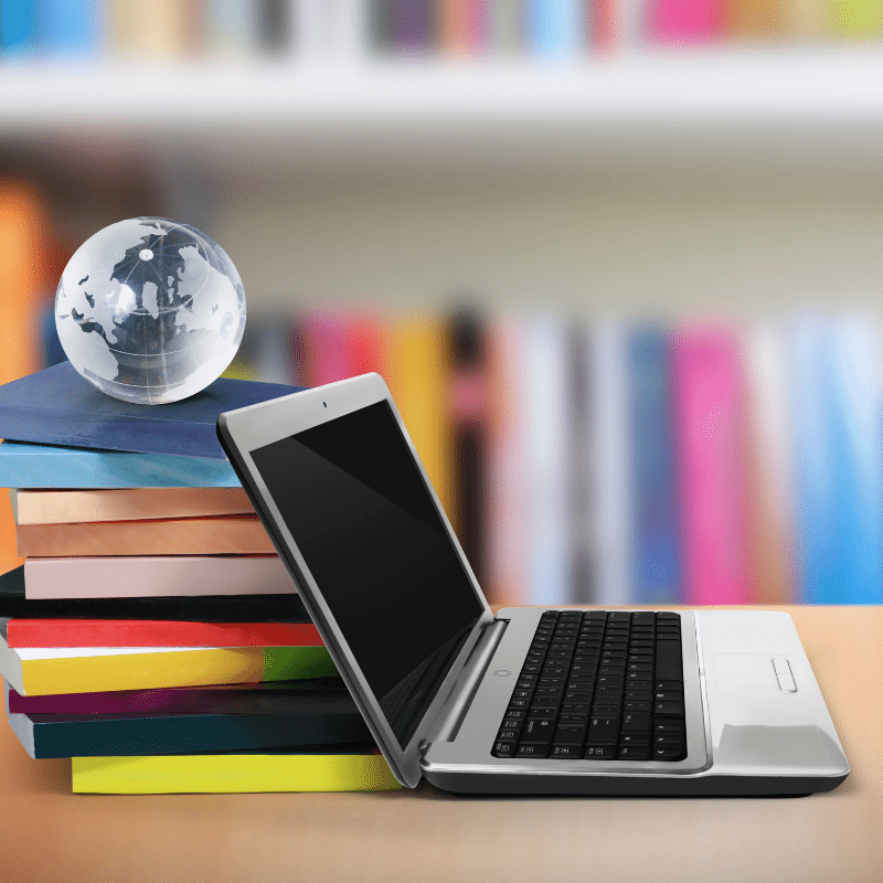 a stack of colorful books lean against an open laptop