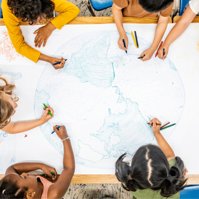 six elementary age students sitting around a table and collectively coloring a large picture of Earth