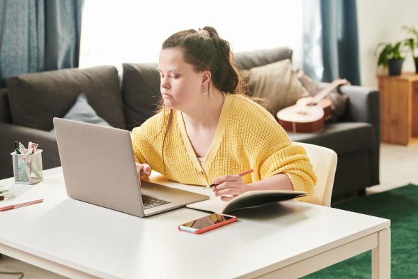 girl with a yellow shirt  using a laptop to complete an assignment