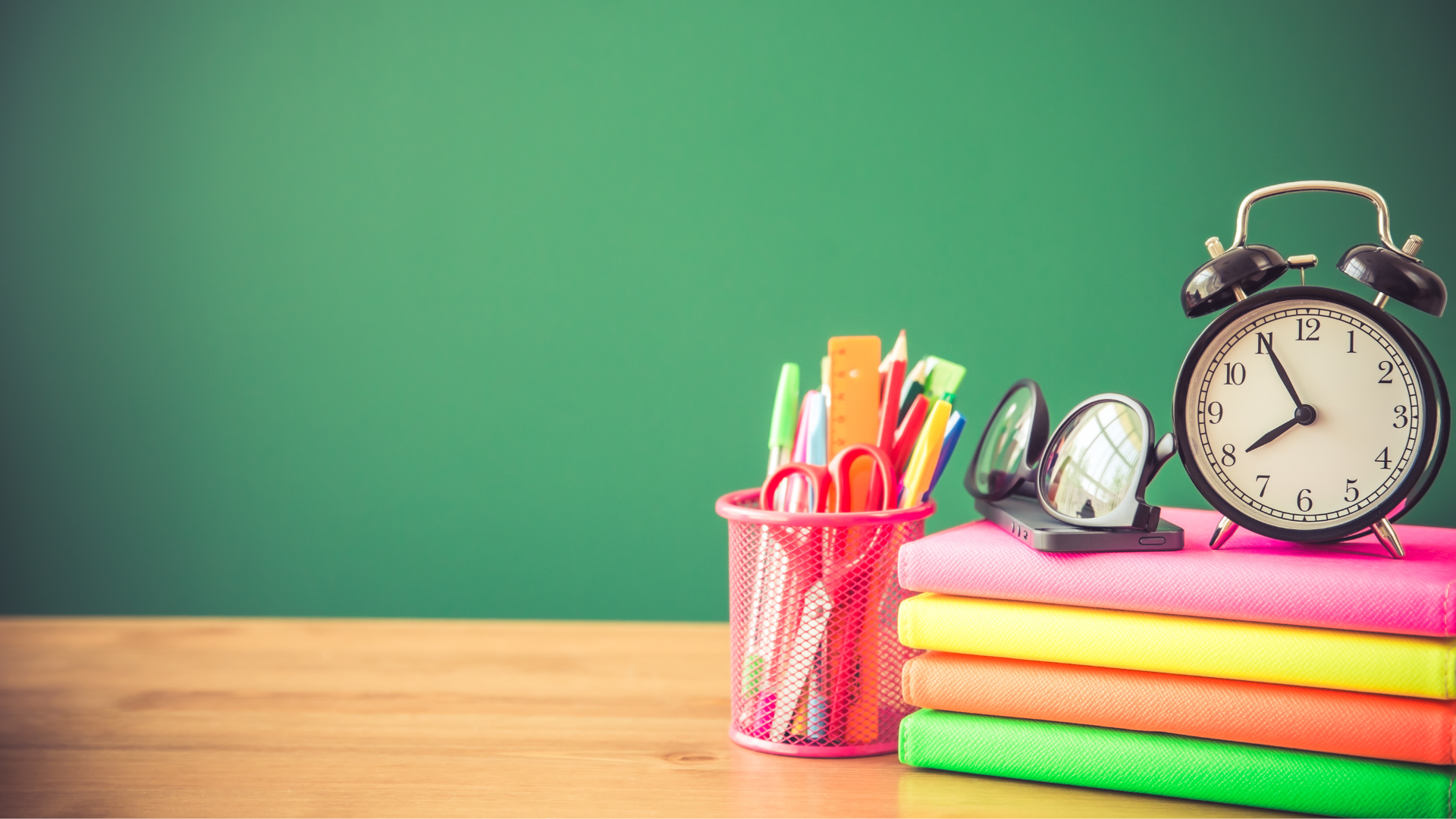 green background with a table that has the following items: pencil cup, glasses, clock, and books
