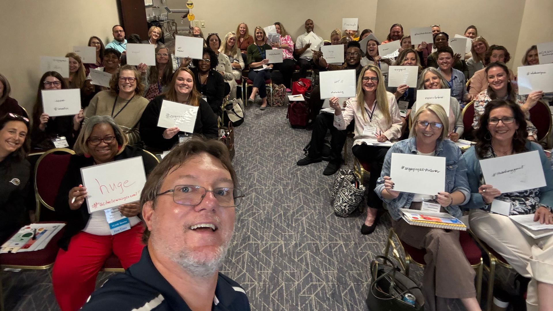 audience at PD smiling and holding up whiteboards