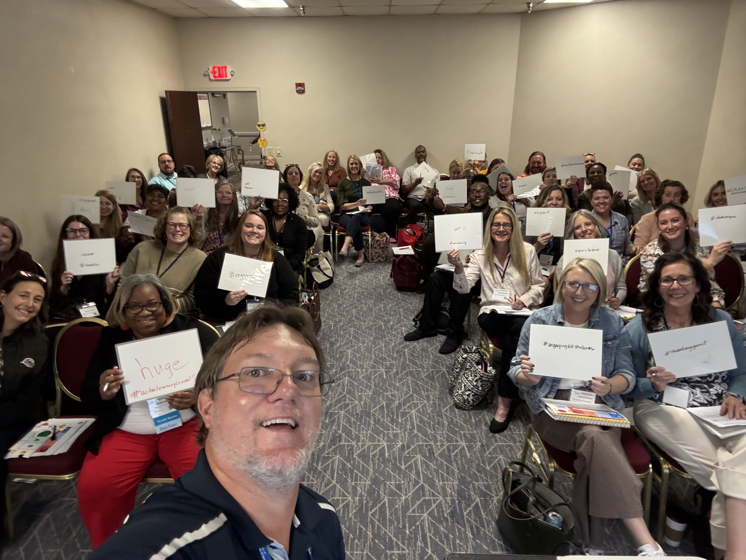audience at PD smiling and holding up whiteboards
