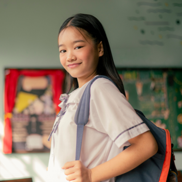 pre-teen female asian student with black backpack faces the camera and smiles
