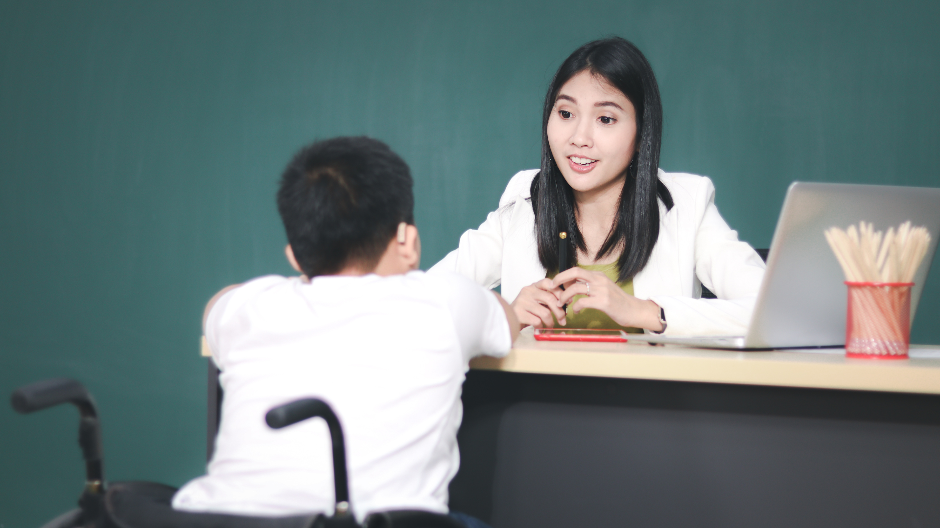 male student who uses a wheelchair is having a conversation with a female teacher